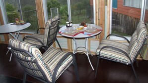A dining area with a table and chairs, a view of trees and a house through large windows. - Fernmark Inn (Brogo)
