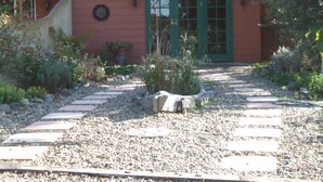 A house with a red exterior, green door, and a garden with a gravel pathway. - Fernmark Inn (Brogo)