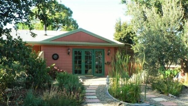 A house with a red exterior, a green door, and a gravel pathway leading to the entrance. - Fernmark Inn (Brogo)