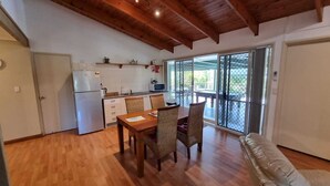 Una cocina amplia con vigas de madera en el techo, un comedor con mesa y sillas, y un ventanal corredero que da a una terraza exterior.