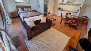 Amplia sala de estar con un sofá grande marrón, una mesa de comedor con sillas, una zona de cocina y un dormitorio con dos camas.