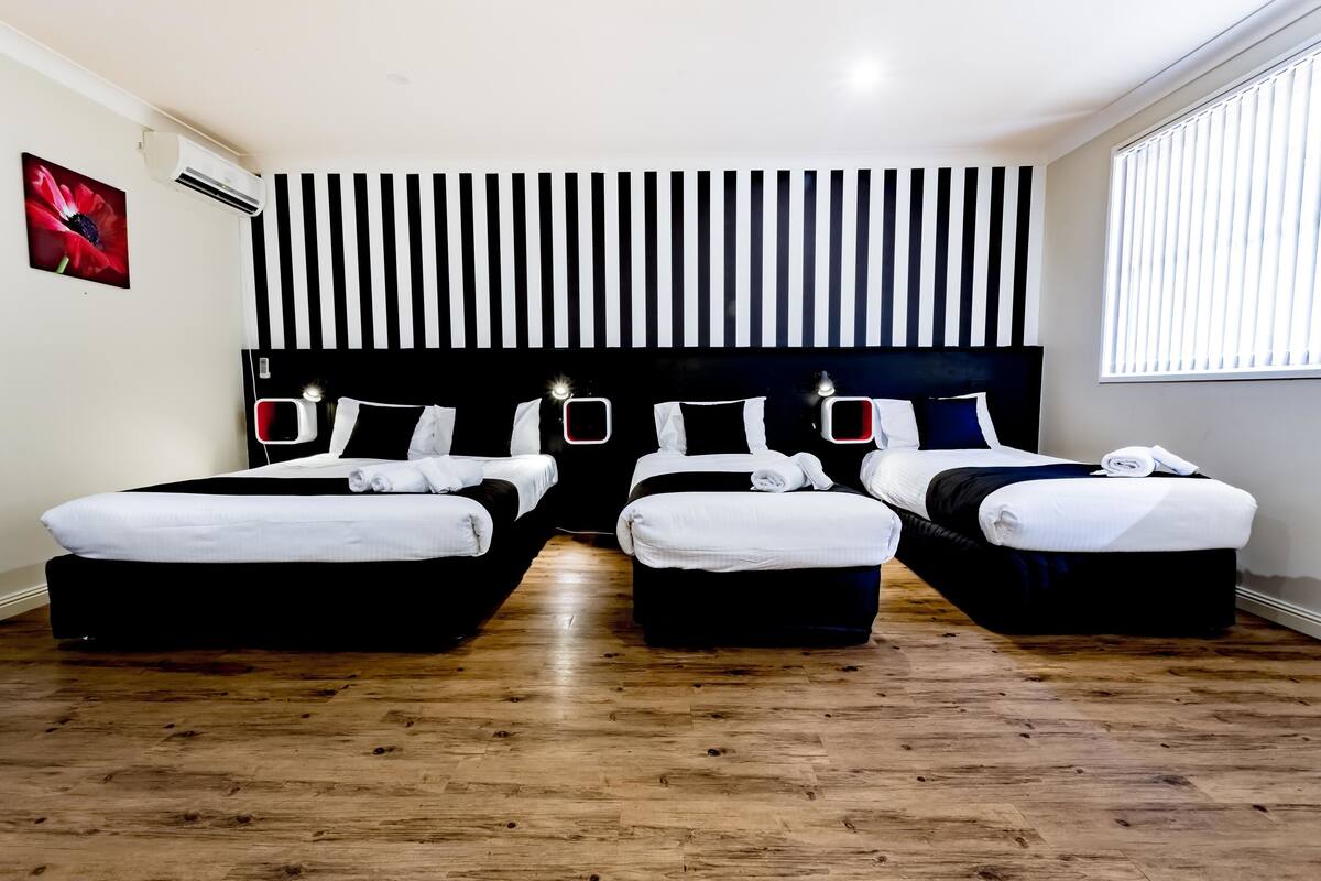A hotel room with two beds, a striped headboard, a wooden floor, and a window with blinds.