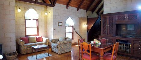 A cozy living room with a wooden ceiling, a fireplace, a dining area with a table and chairs, and a kitchen with wooden cabinets.