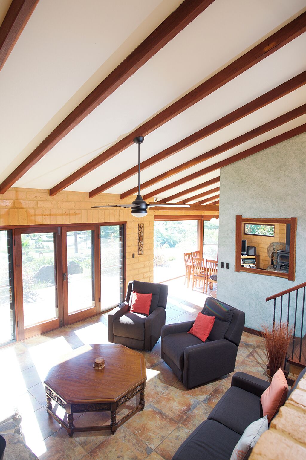 Un'ampia zona giorno con soffitto alto, travi in legno e grandi porte scorrevoli in vetro che si aprono su un patio esterno.