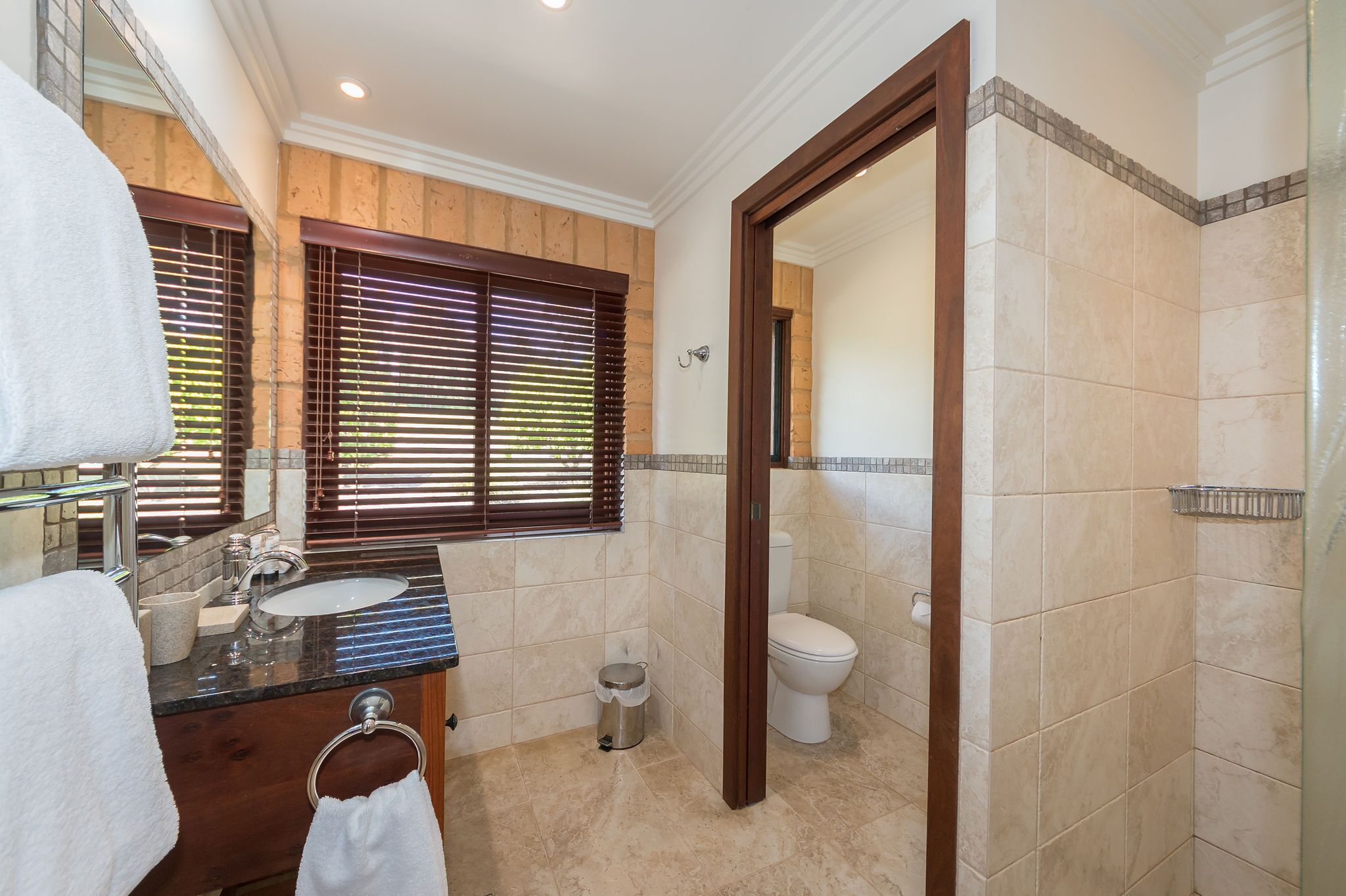 Une salle de bain avec un meuble-lavabo en bois, deux vasques, des toilettes et un espace douche.