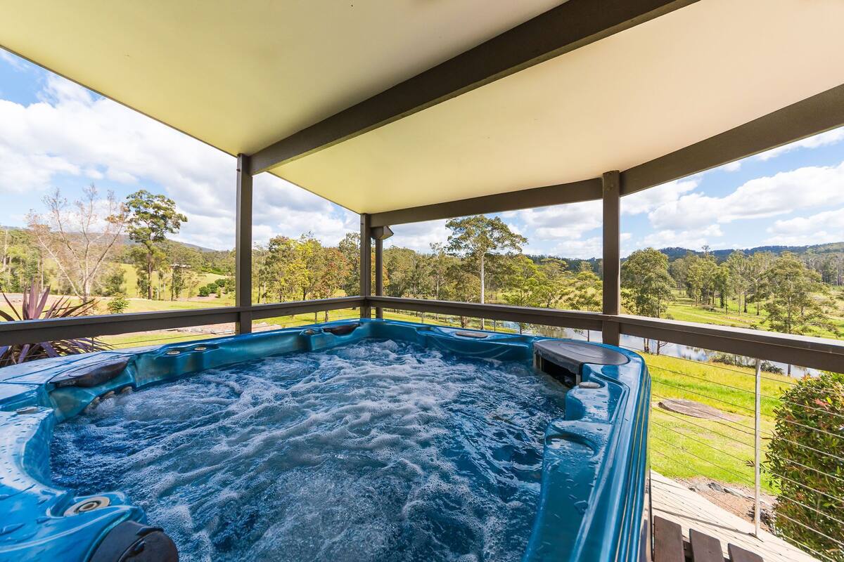 A hot tub on a covered balcony with a view of a green landscape.