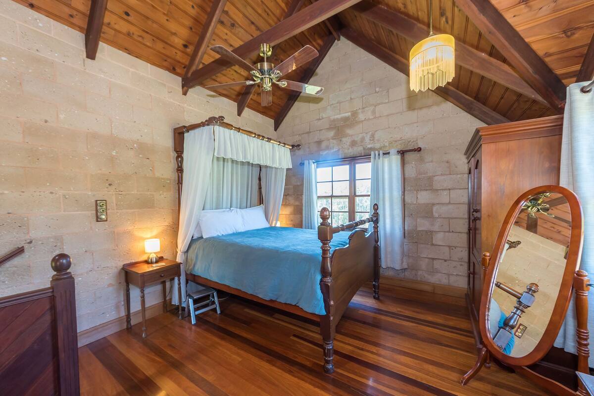A bedroom with a wooden bed, a nightstand, a mirror, and a window with curtains.