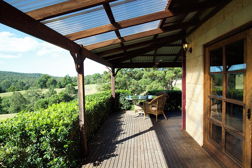 A covered outdoor area with a wooden deck, a table with chairs, and a view of a green landscape.