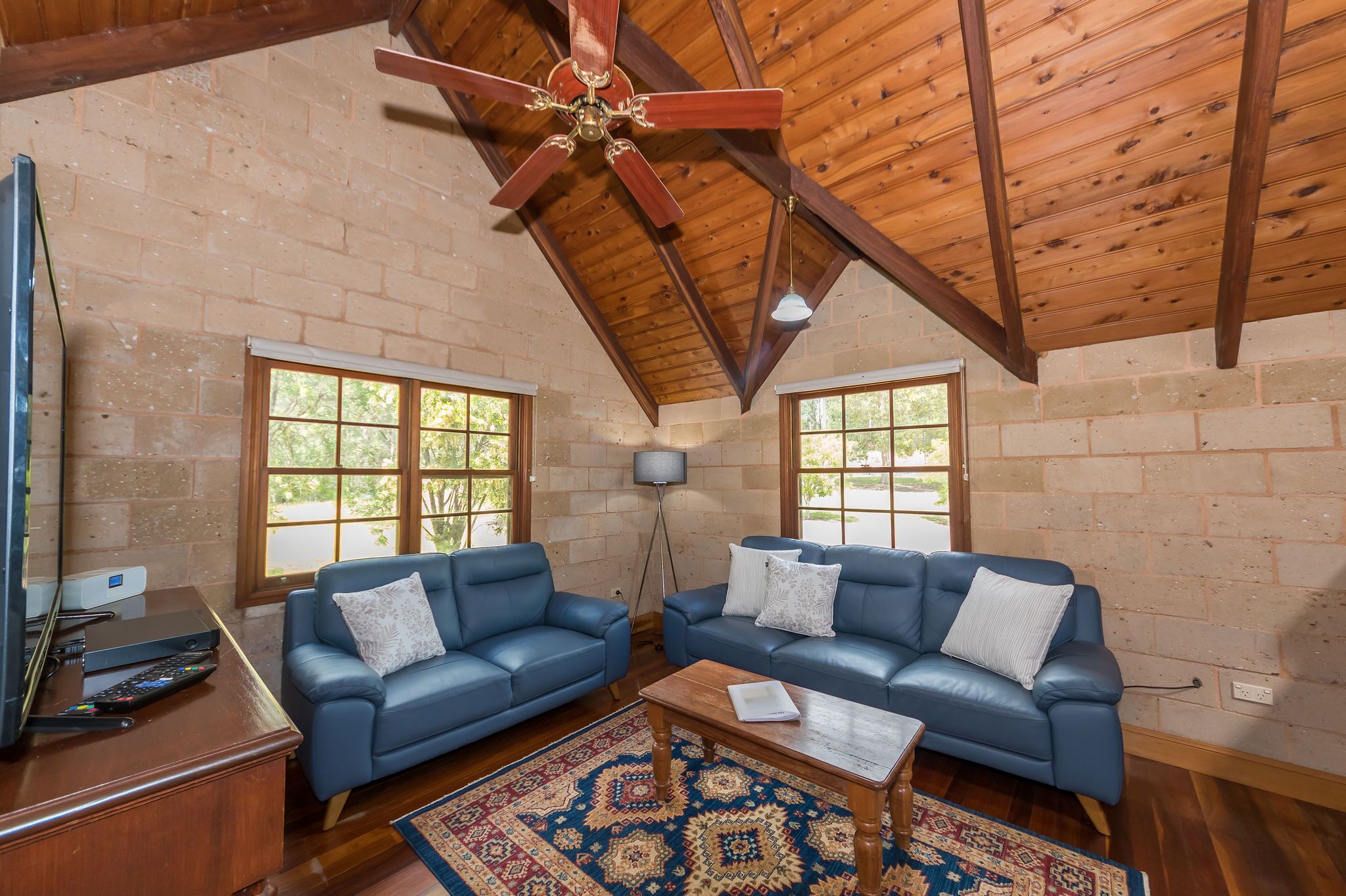 A spacious living room with two blue sofas, a wooden coffee table, and a ceiling fan.
