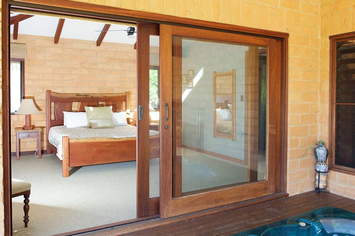 A bedroom with a large sliding glass door leading to a balcony, a wooden bed, and a hot tub on the balcony.