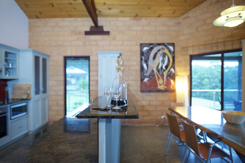 A kitchen with a dining area, featuring a brick wall, wooden ceiling, and large windows.