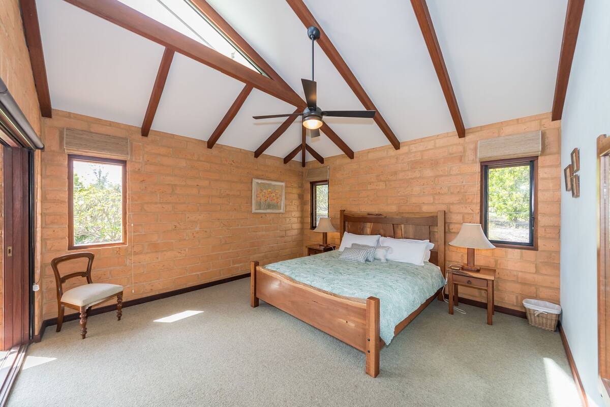 A bedroom with a wooden bed, a ceiling fan, a window, and a chair.