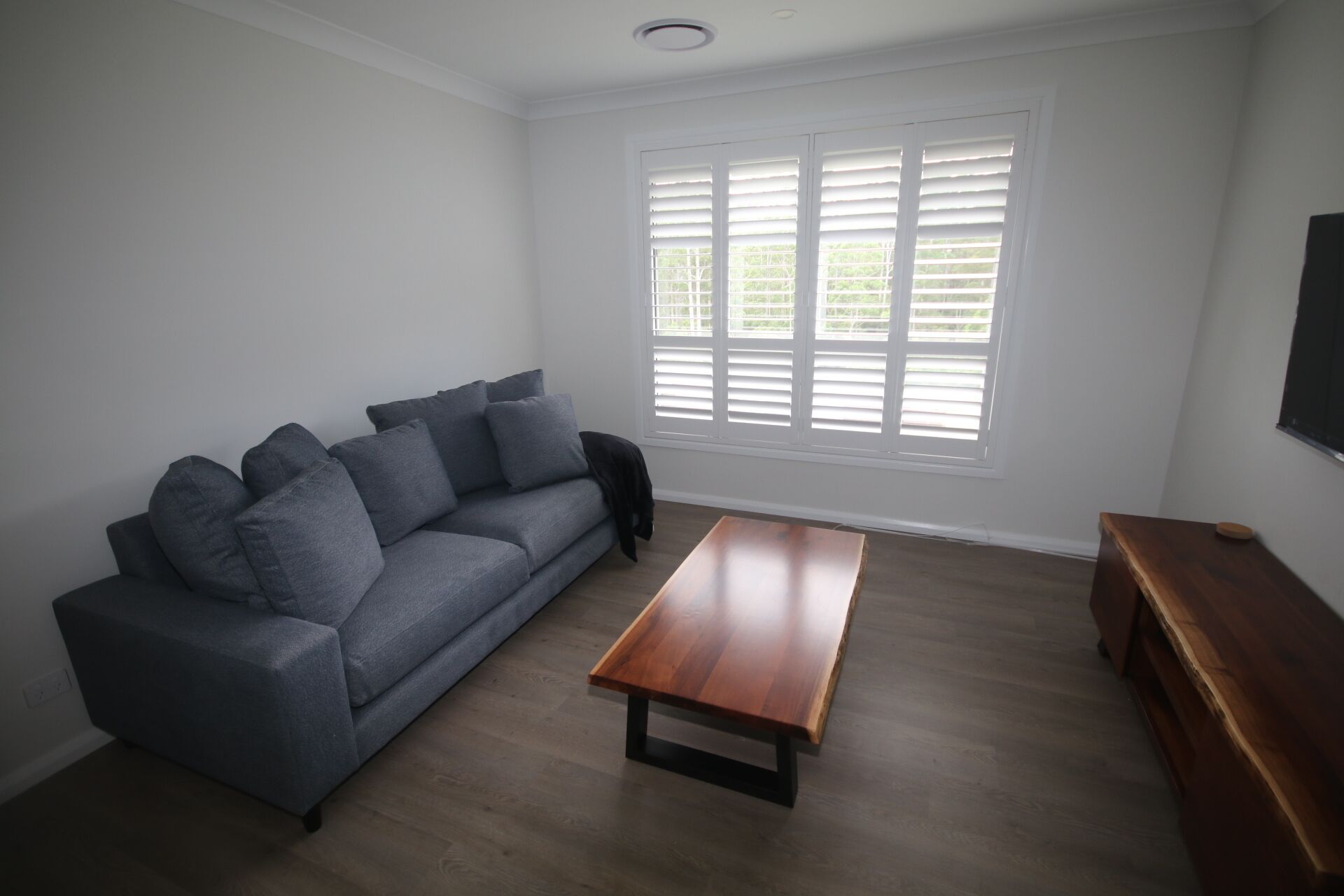 A living room with a grey sofa, a wooden coffee table, and a TV on the wall.