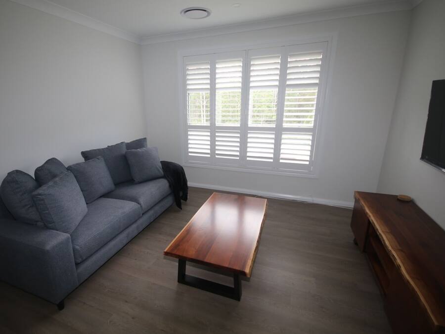 A living room with a grey sofa, a wooden coffee table, and a TV on the wall.