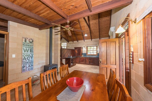 Una mesa de comedor de madera con sillas, un tazón rojo y un ventilador de techo en una cocina y comedor rústicos.