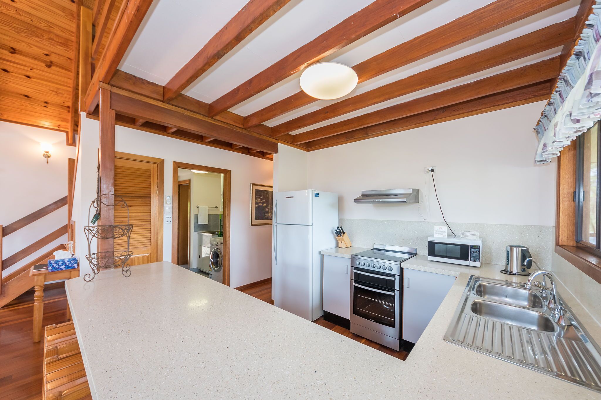 Una cucina con travi in legno, un piano di lavoro bianco, elettrodomestici in acciaio inossidabile e un lavello.