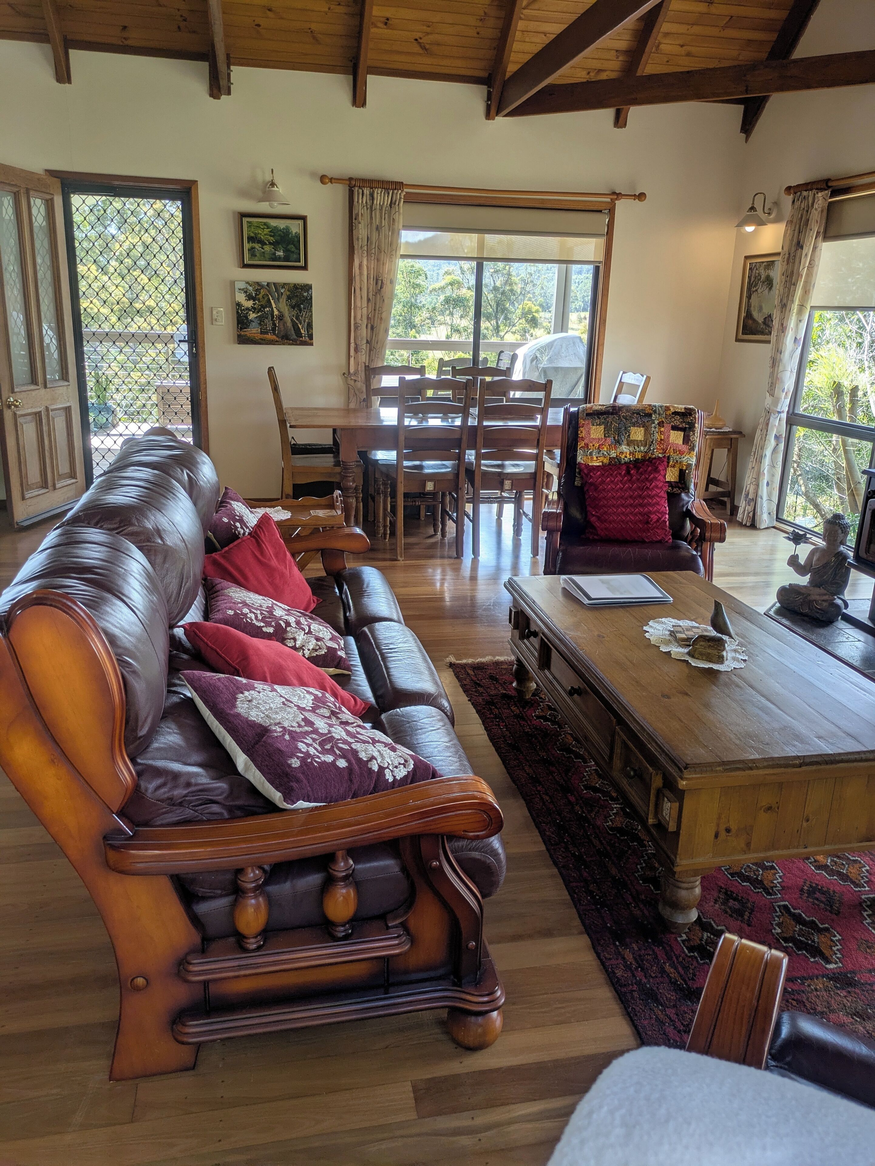 A cozy living room with a leather sofa, wooden coffee table, and a dining area with a wooden table and chairs.