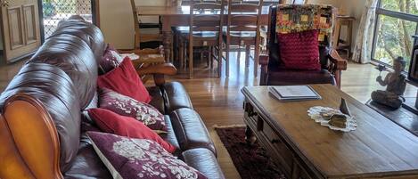 A cozy living room with a leather sofa, wooden coffee table, and a dining area with a wooden table and chairs.