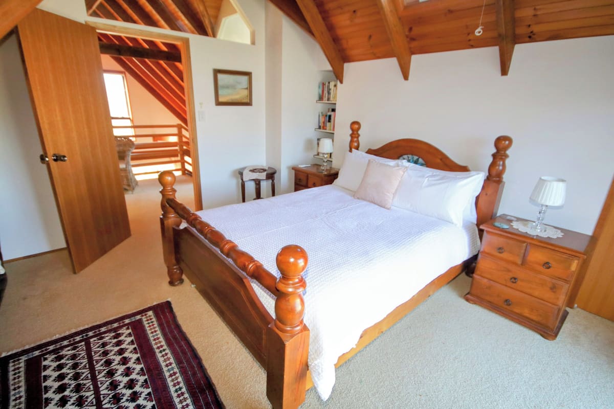 A bedroom with a wooden bed, a nightstand, a bedside table, a rug, and a staircase leading to an upper level.