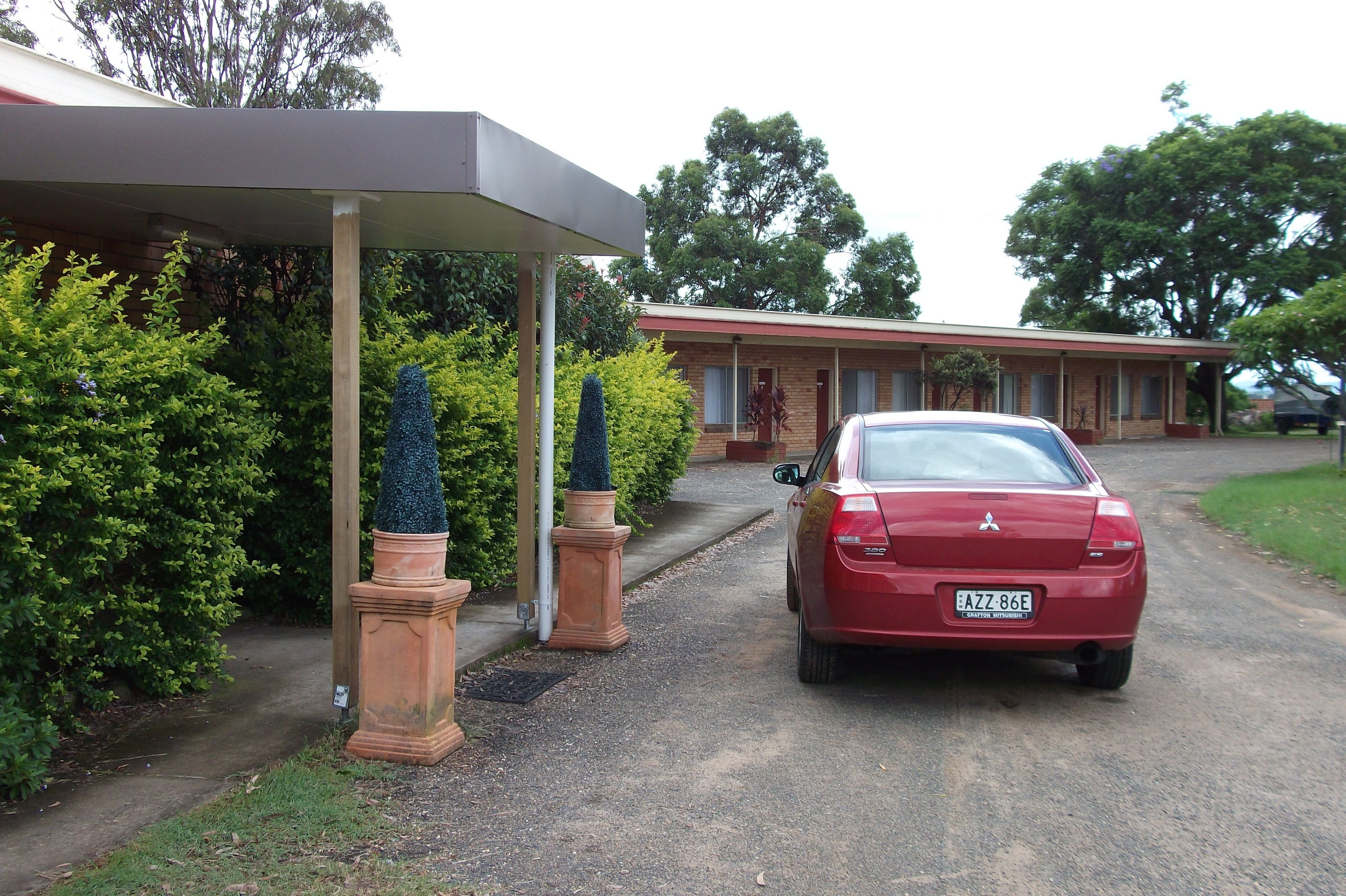 A red car parked in front of a building with a covered walkway and a brick facade.