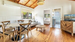 Una habitación amplia con techo de madera, una mesa de comedor redonda con sillas, un sofá, una pequeña mesa de centro y un televisor sobre un mueble de madera.