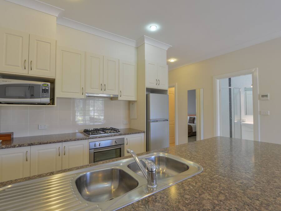 A kitchen with white cabinets, a stainless steel sink, a microwave, a stove, and a refrigerator.