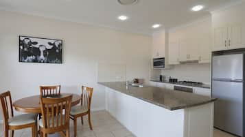 Cocina moderna con armarios blancos, un refrigerador de acero inoxidable, microondas y comedor con sillas y mesa de madera.