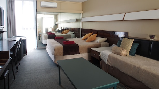 A hotel room with two beds, a desk, a chair, and a bench. - City Beach Motel (Wollongong)