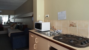 A compact kitchen with a microwave, stove, and sink. There is a sofa in the adjacent living area. - City Beach Motel (Wollongong)