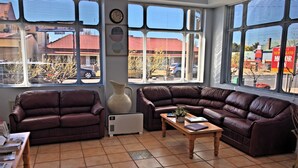 A living room with two leather sofas, a coffee table, and a radiator. There are large windows with blinds, a clock on the wall, and a vase on the floor. - New England Motor Inn (Armidale)