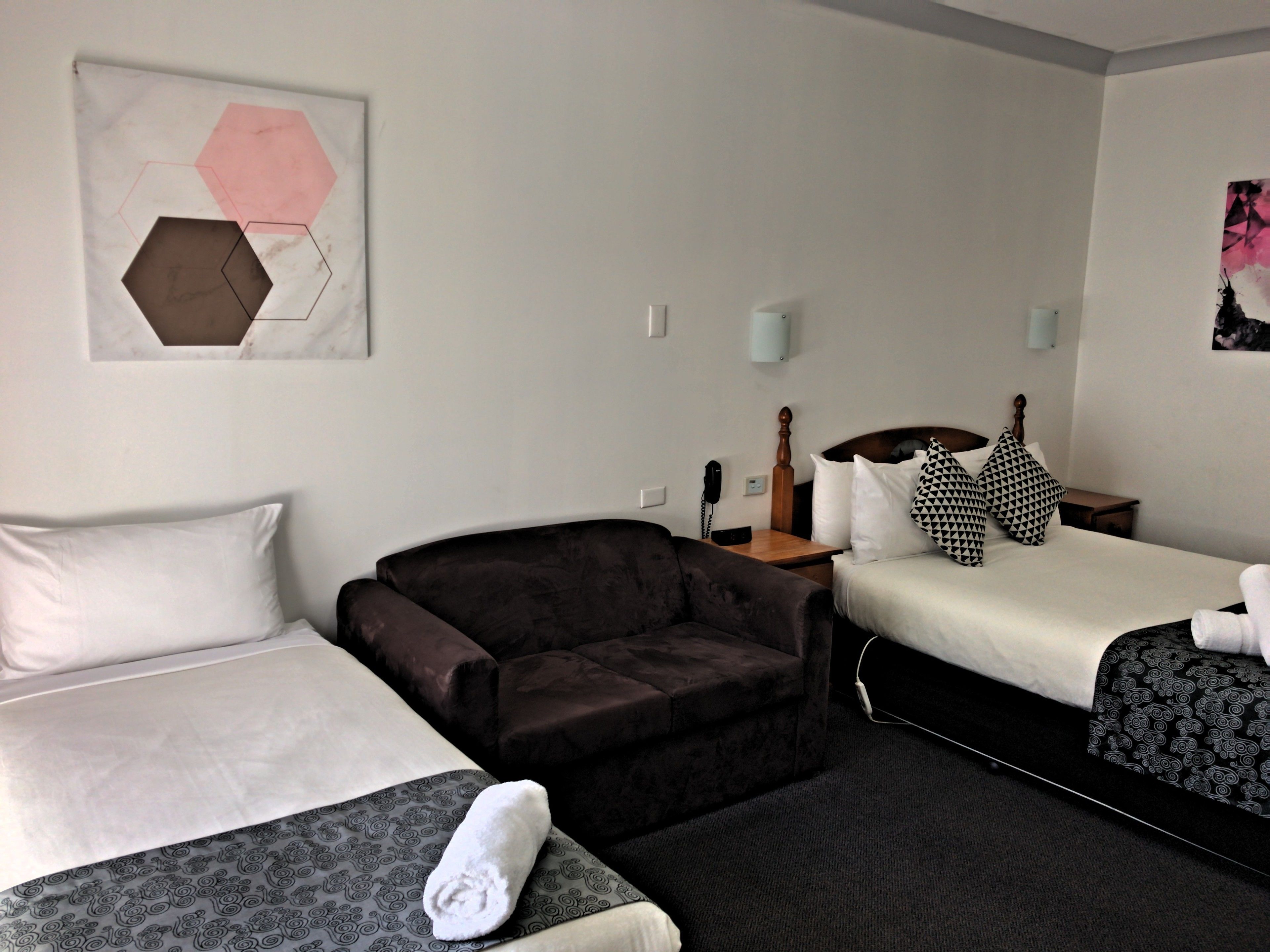 A hotel room with a bed, a sofa, and a chair. There is a painting on the wall and a lamp on the nightstand.