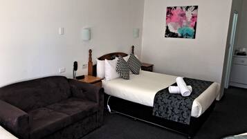 Quarto de hotel com cama, um sofá marrom escuro, mesa de cabeceira com abajur, telefone e um quadro na parede.