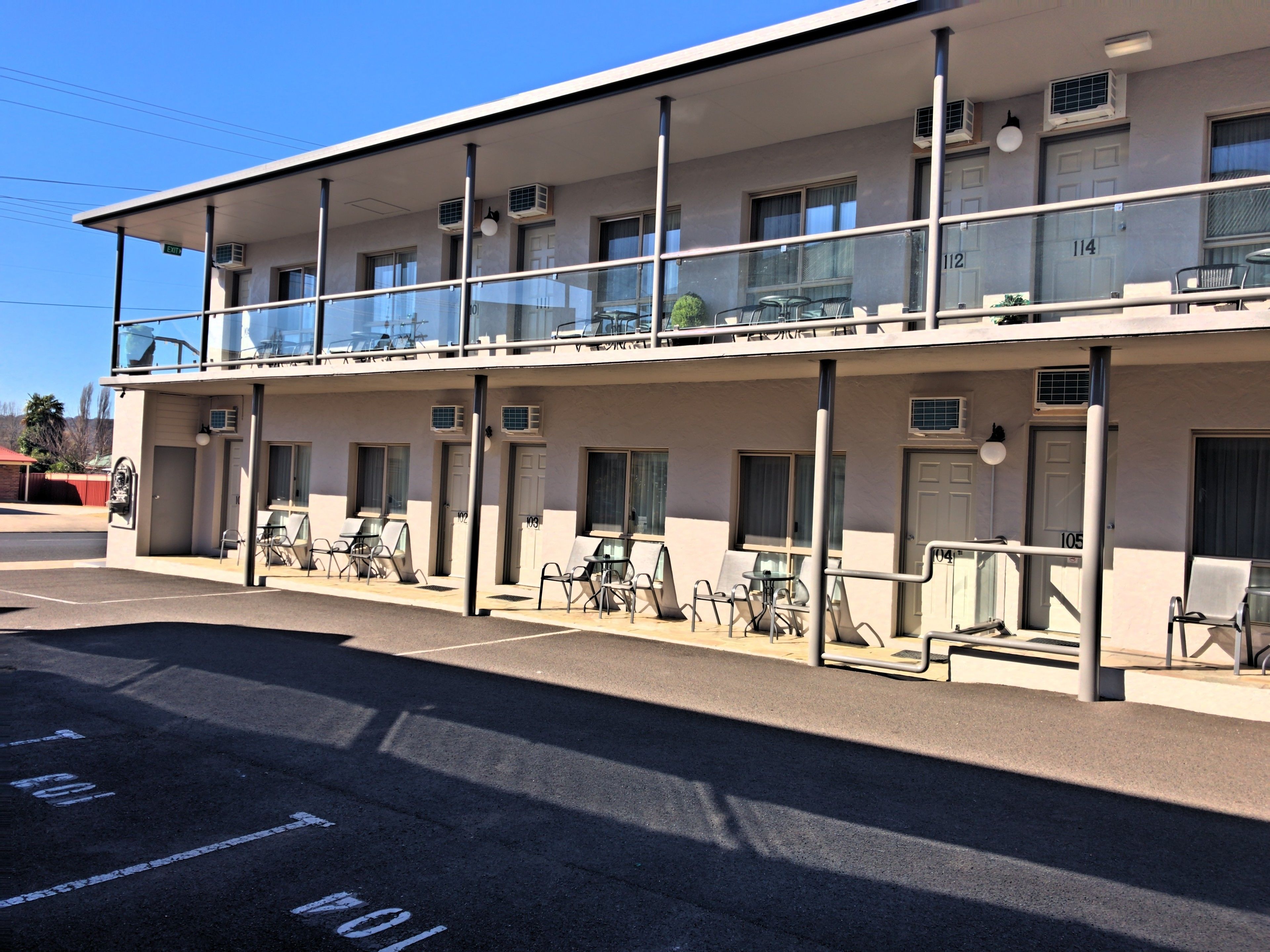A two-story motel with a covered outdoor seating area and multiple air conditioning units.