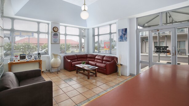A spacious living area with a red leather sofa, a wooden coffee table, and a large window offering a view of the city. - New England Motor Inn (Armidale)
