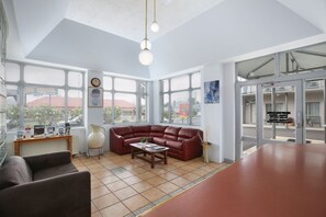 A spacious living area with a red leather sofa, a wooden coffee table, and a large window offering a view of the city.