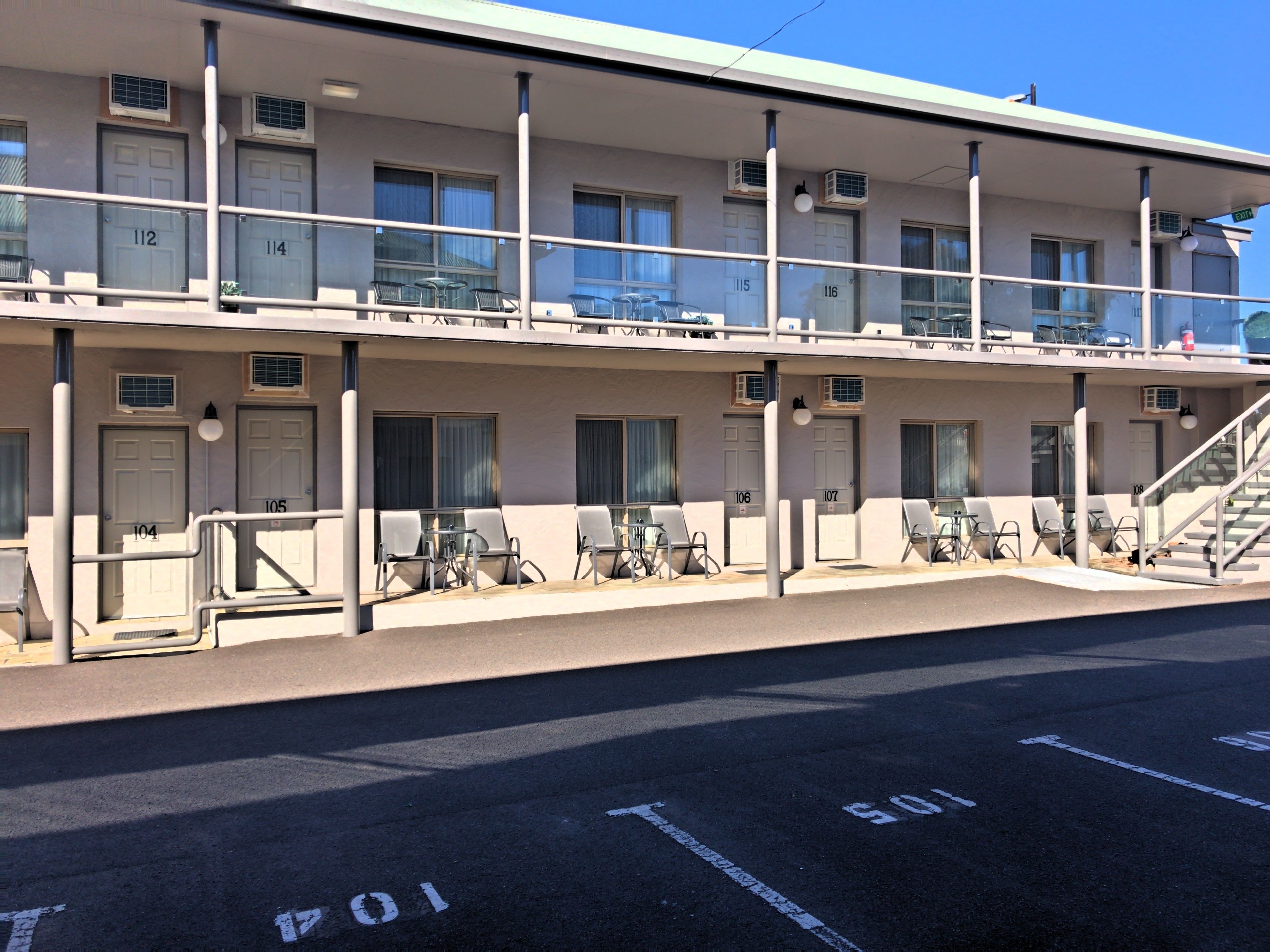 Un motel con habitaciones numeradas, asientos exteriores y una escalera que conduce al nivel superior.