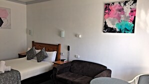 A hotel room with two beds, a sofa, a small table, and a painting on the wall. - New England Motor Inn (Armidale)