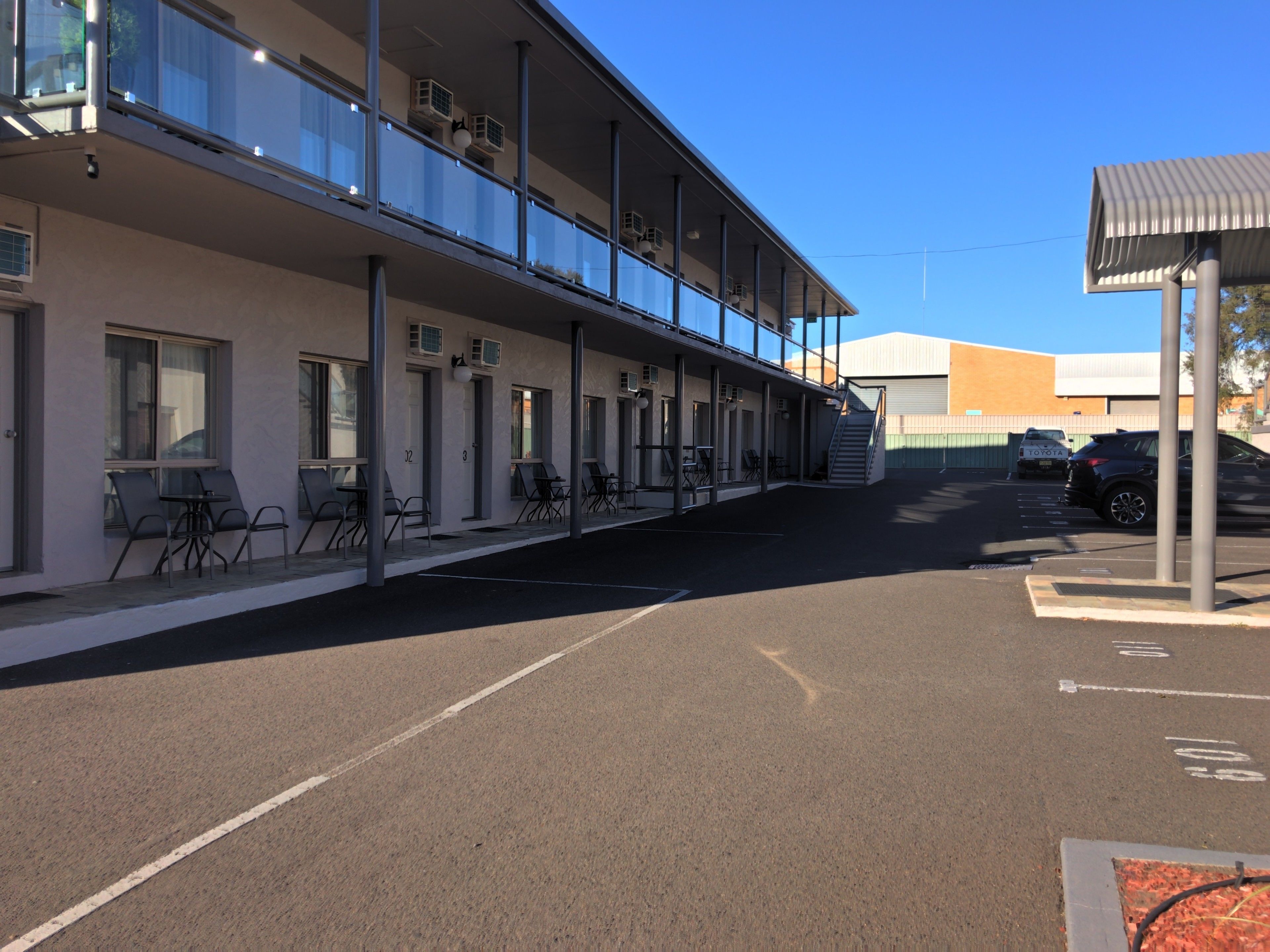 Un motel con mesas al aire libre, un espacio cubierto y estacionamiento.