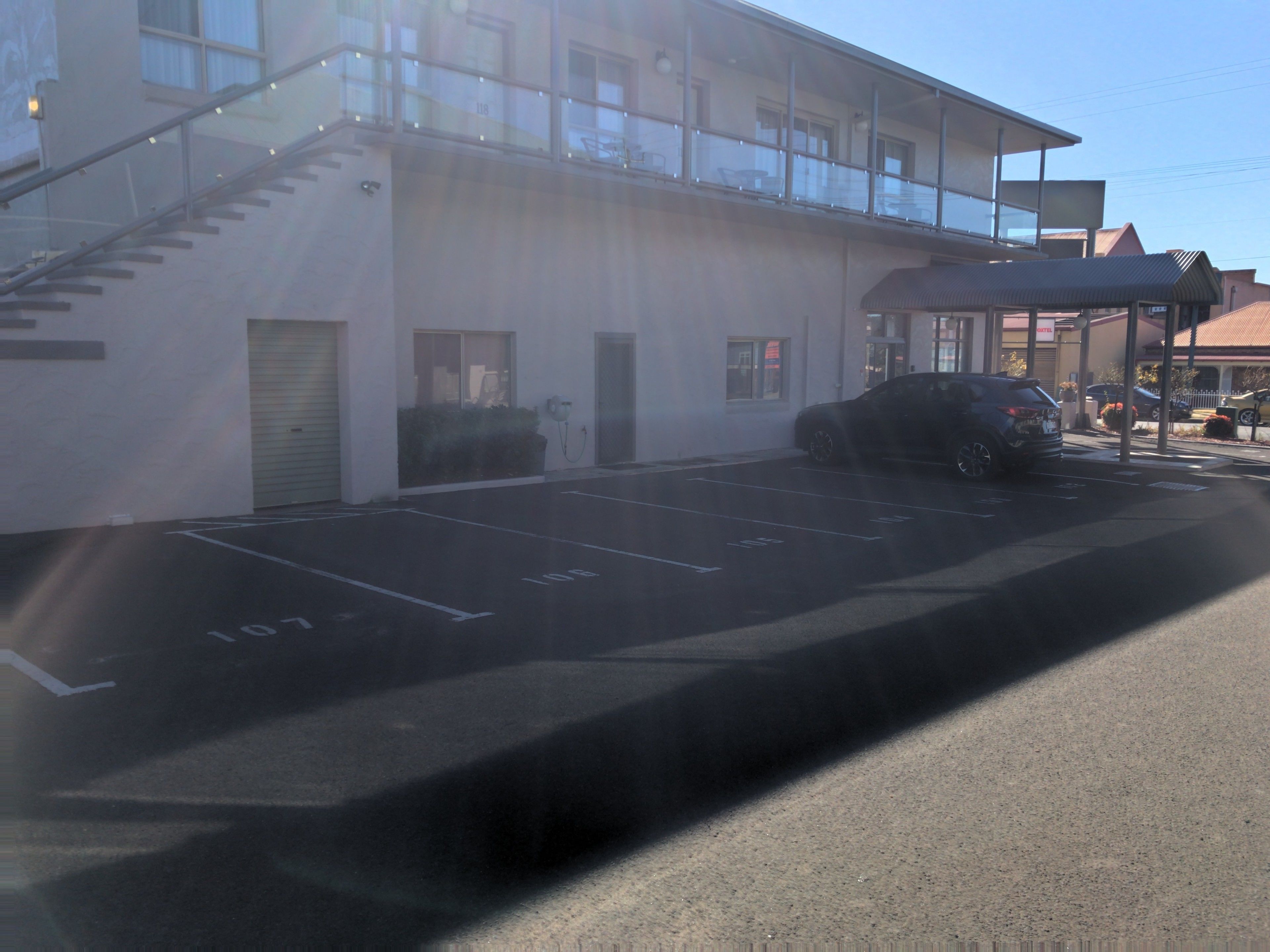 Un parking avec des places délimitées, un bâtiment doté d’un balcon et une voiture garée sur le parking.