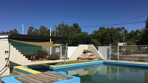 A swimming pool with blue and yellow painted edges, surrounded by a fenced area with steps leading up to a white building. - Boggabilla Motel (Boggabilla)