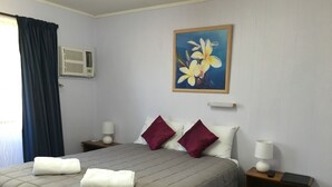 A hotel room with a bed, two nightstands, a painting, and an air conditioning unit. - Boggabilla Motel (Boggabilla)