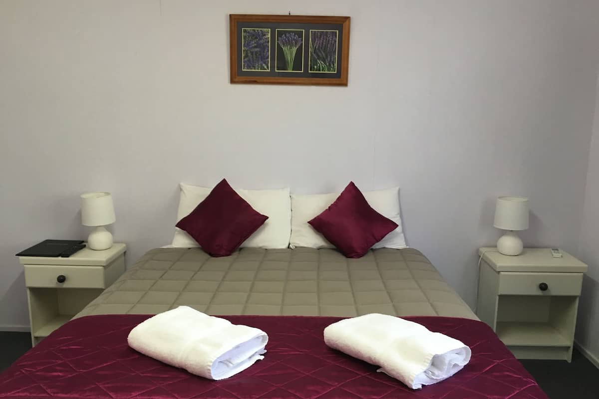 A hotel room with a bed, two pillows, two nightstands with lamps, and a framed picture on the wall.