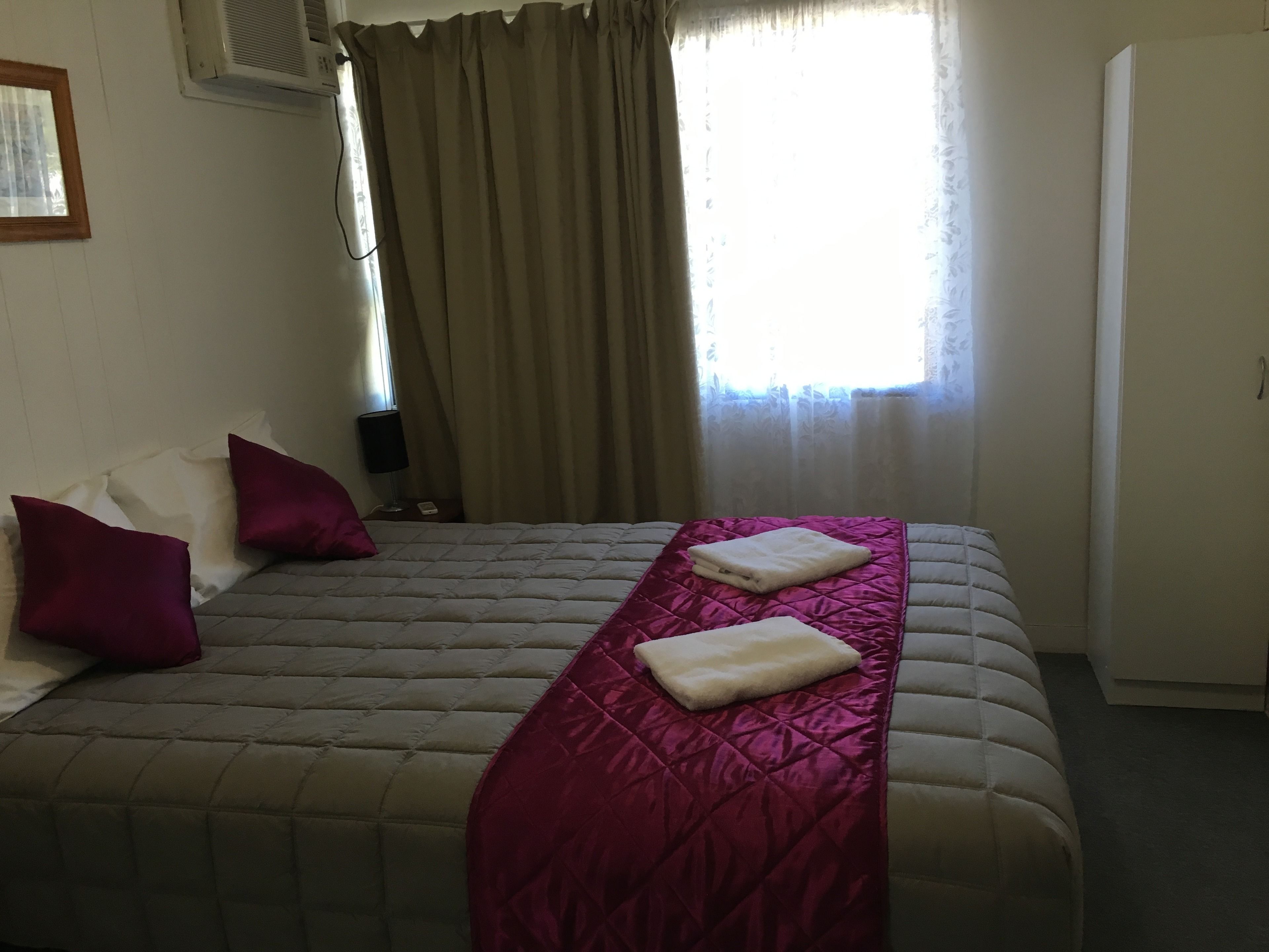 A neatly made bed with a quilted headboard, two pillows, and a folded towel.