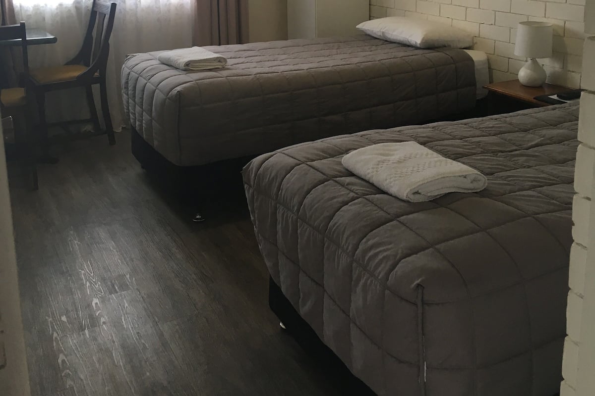 A room with two beds, a desk, a chair, a wardrobe, and a painting on the wall.