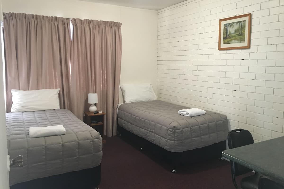A hotel room with two beds, a nightstand with a lamp, a painting on the wall, and a table.