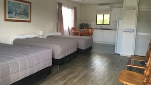 A room with two beds, a dining table, a kitchen area, and a painting on the wall. - Boggabilla Motel (Boggabilla)