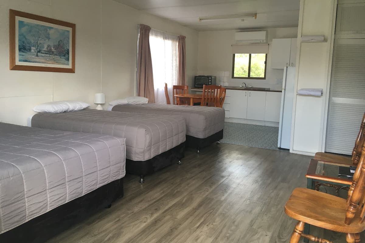 A room with two beds, a dining table, a kitchen area, and a painting on the wall.