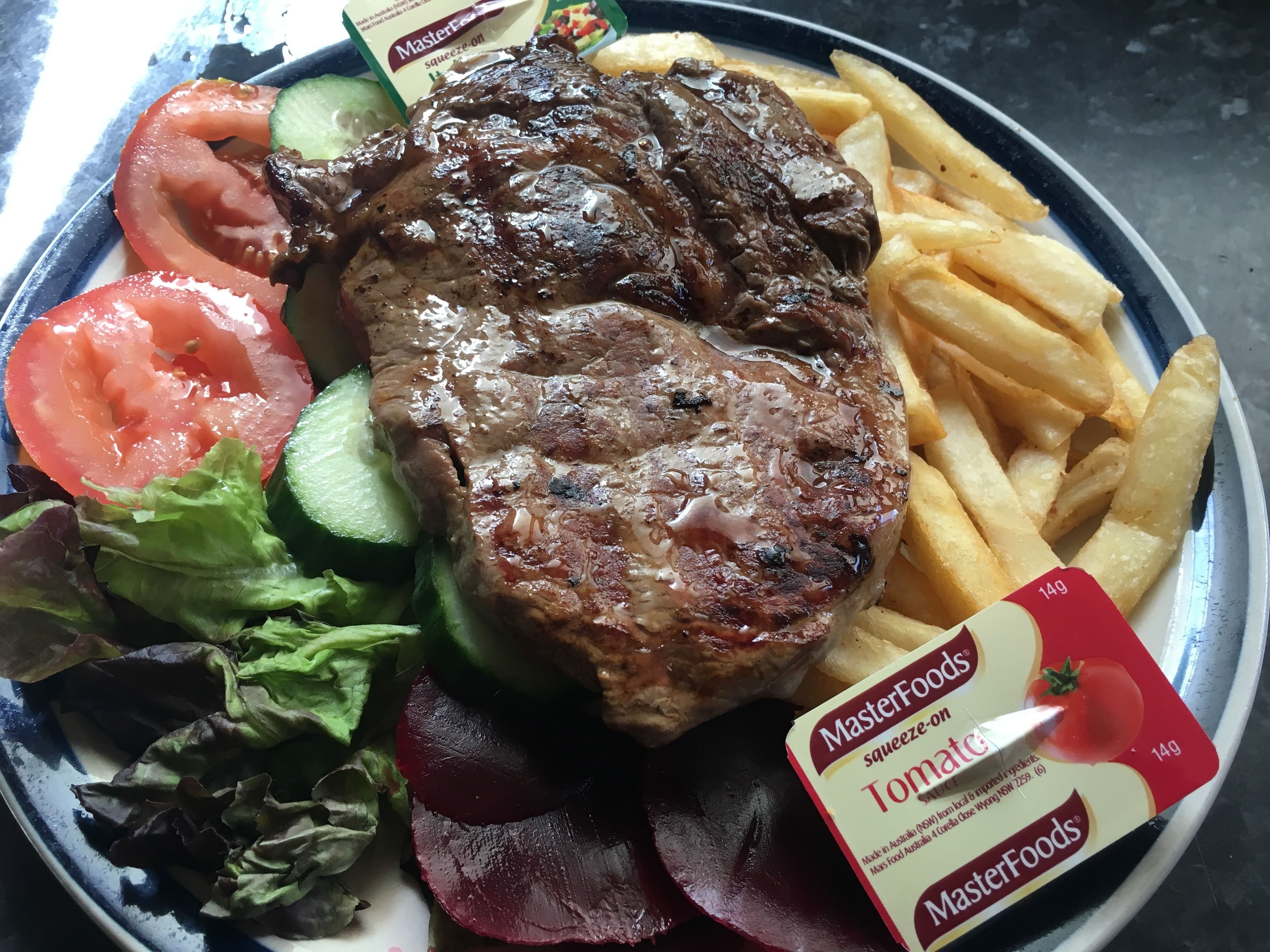 Un plato con un bistec, papas fritas y verduras, incluyendo lechuga, tomate y pepino.