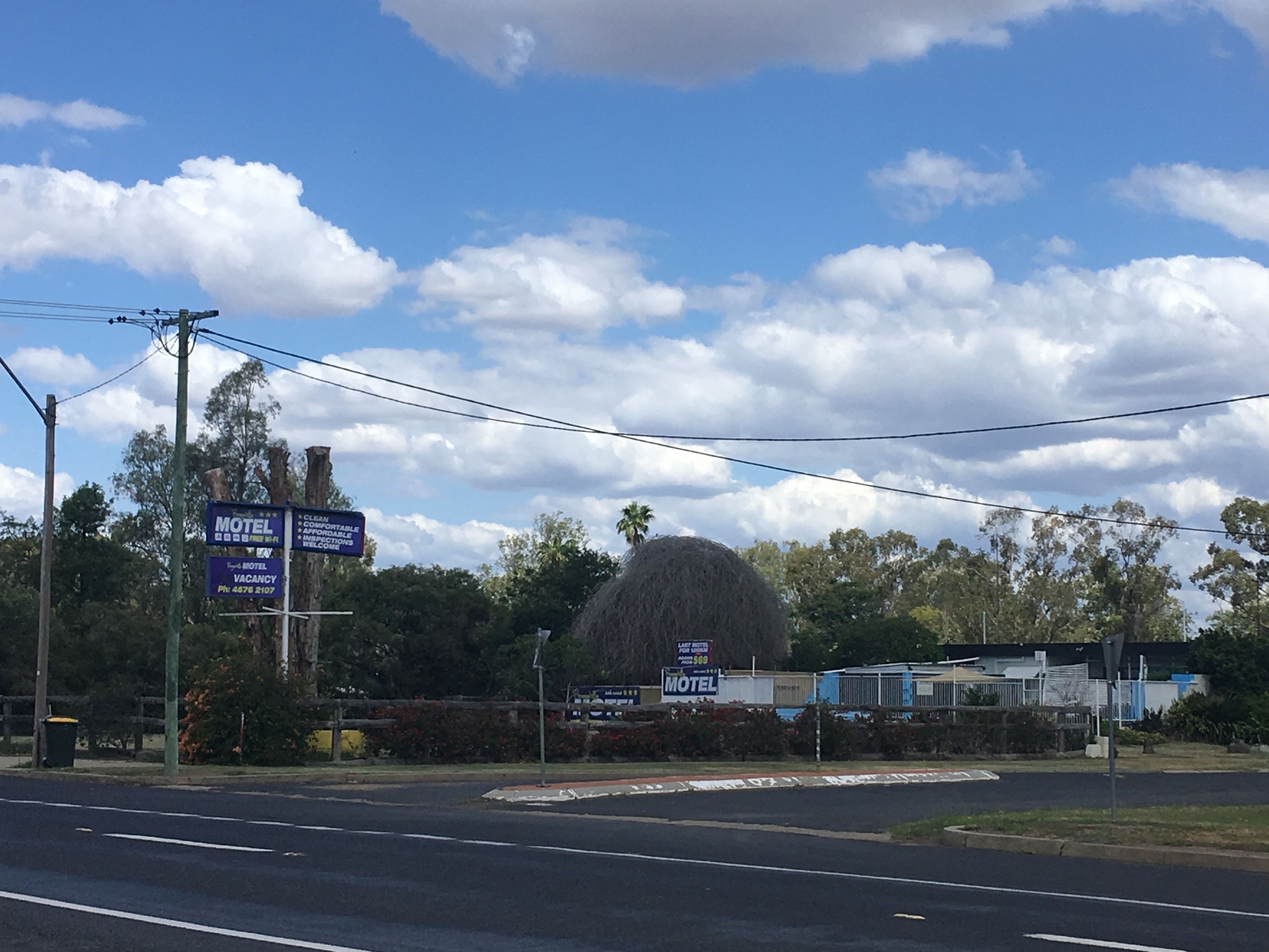 A motel with a large signboard, a parking area, and a clear sky with clouds.
