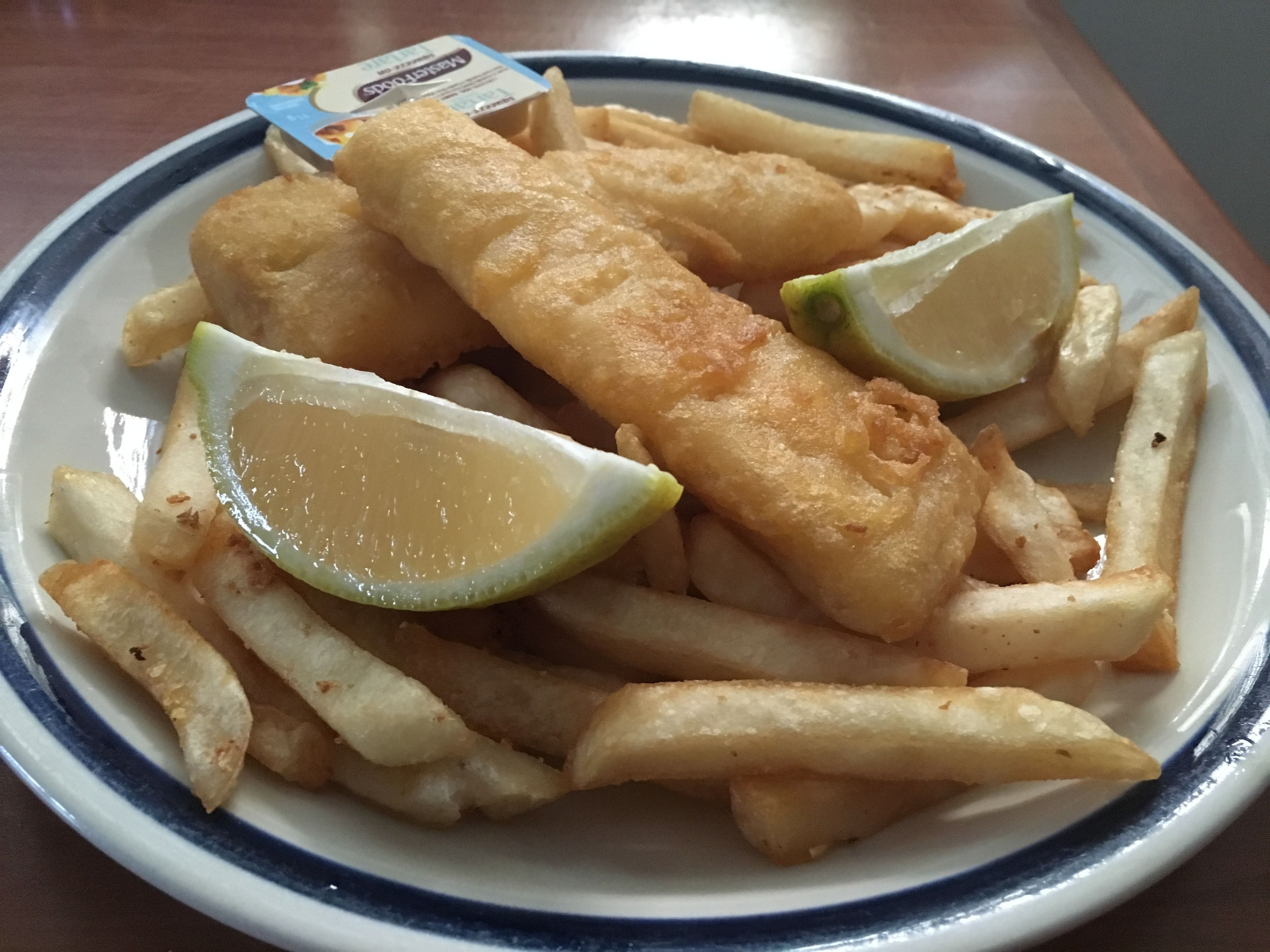 Un plato de pescado y papas fritas con gajos de limón y una salsita tártara.